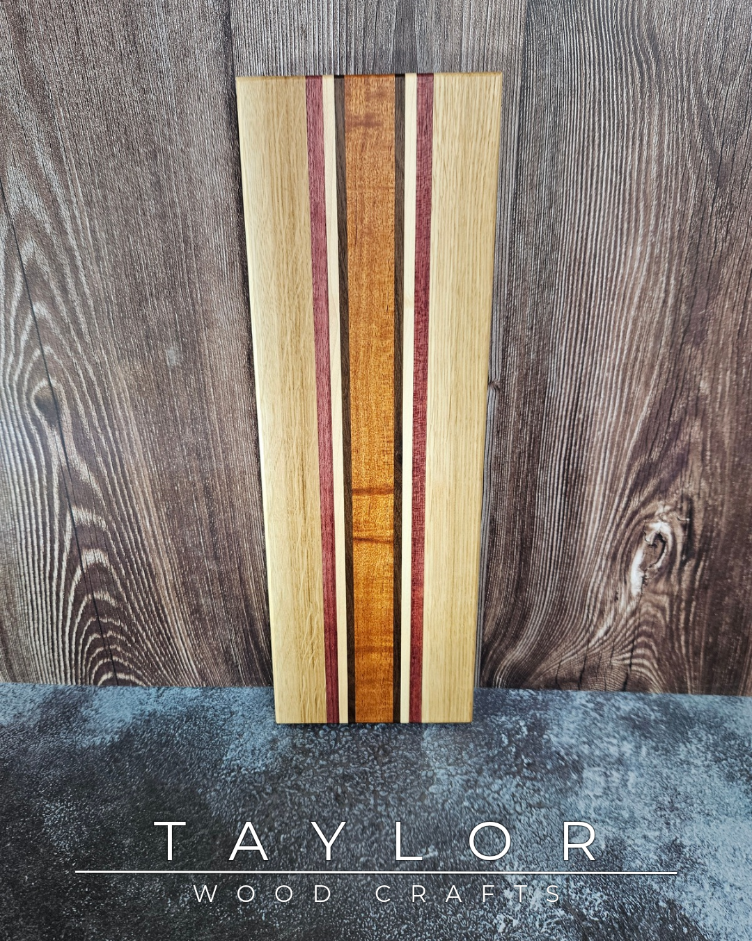 Wooden cutting board with multicolored stripes on a wooden surface, branded 'Taylor Wood Craft'.