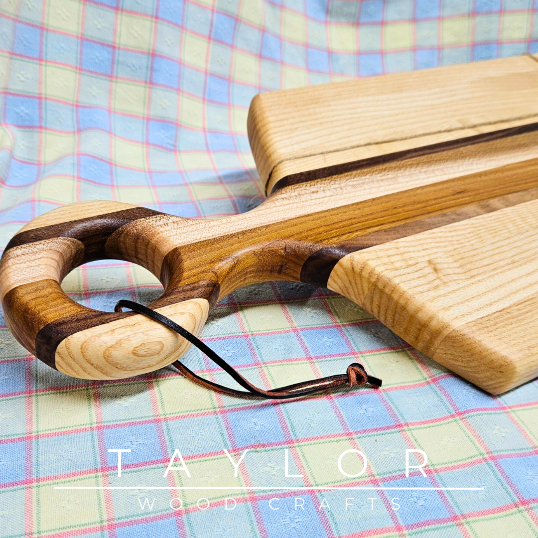 Handcrafted paddle board made with elm, ash, and walnut, featuring a leather string for hanging, combining durability and rustic style.