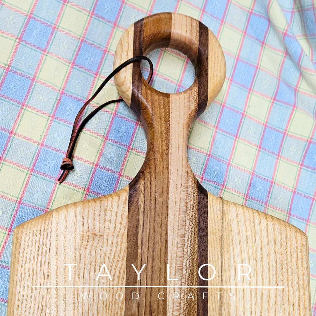 Handcrafted paddle board made with elm, ash, and walnut, featuring a leather string for hanging, combining durability and rustic style.