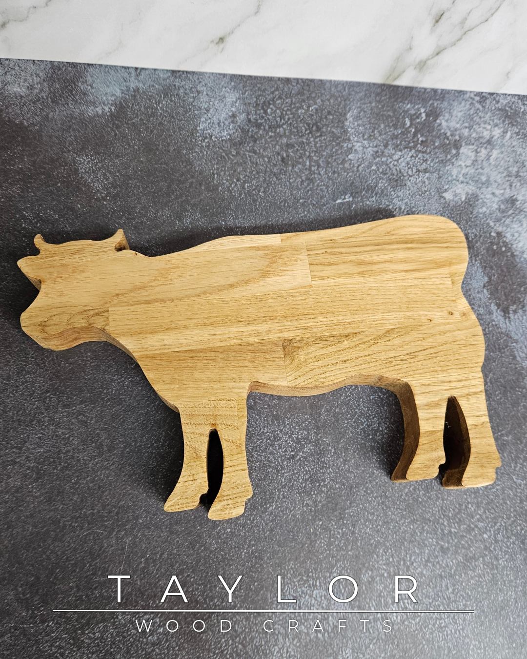 Wooden cow-shaped cutting board on a gray surface with 'Taylor Wood Crafts' branding.