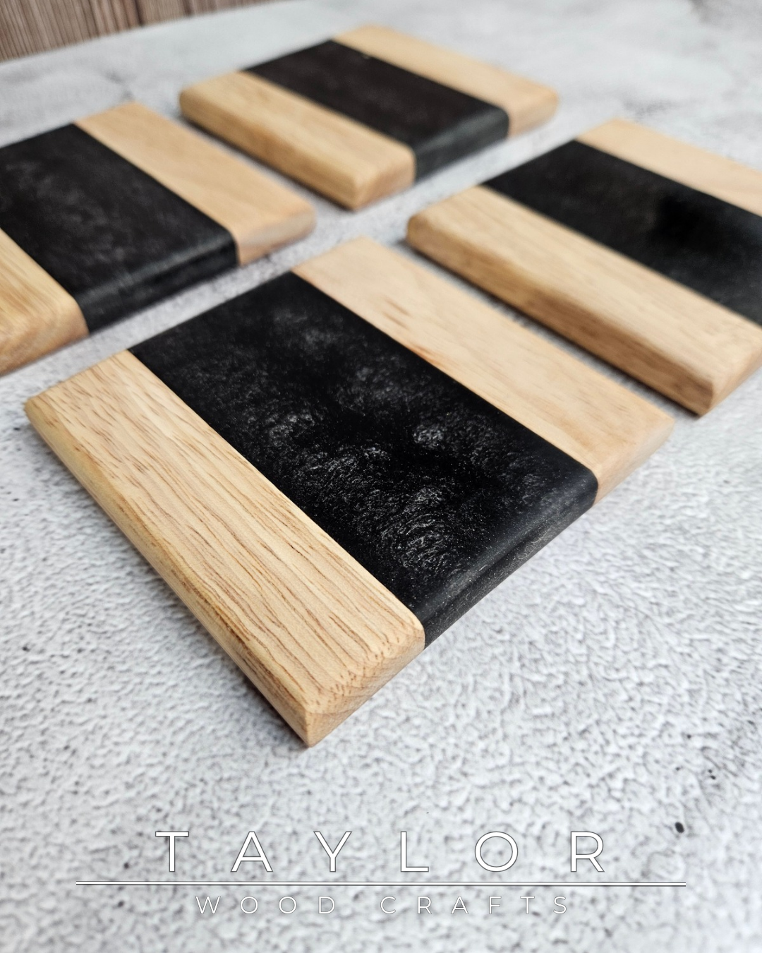 Set of four black and wooden coasters on a textured surface with 'Taylor Woodwork' branding.