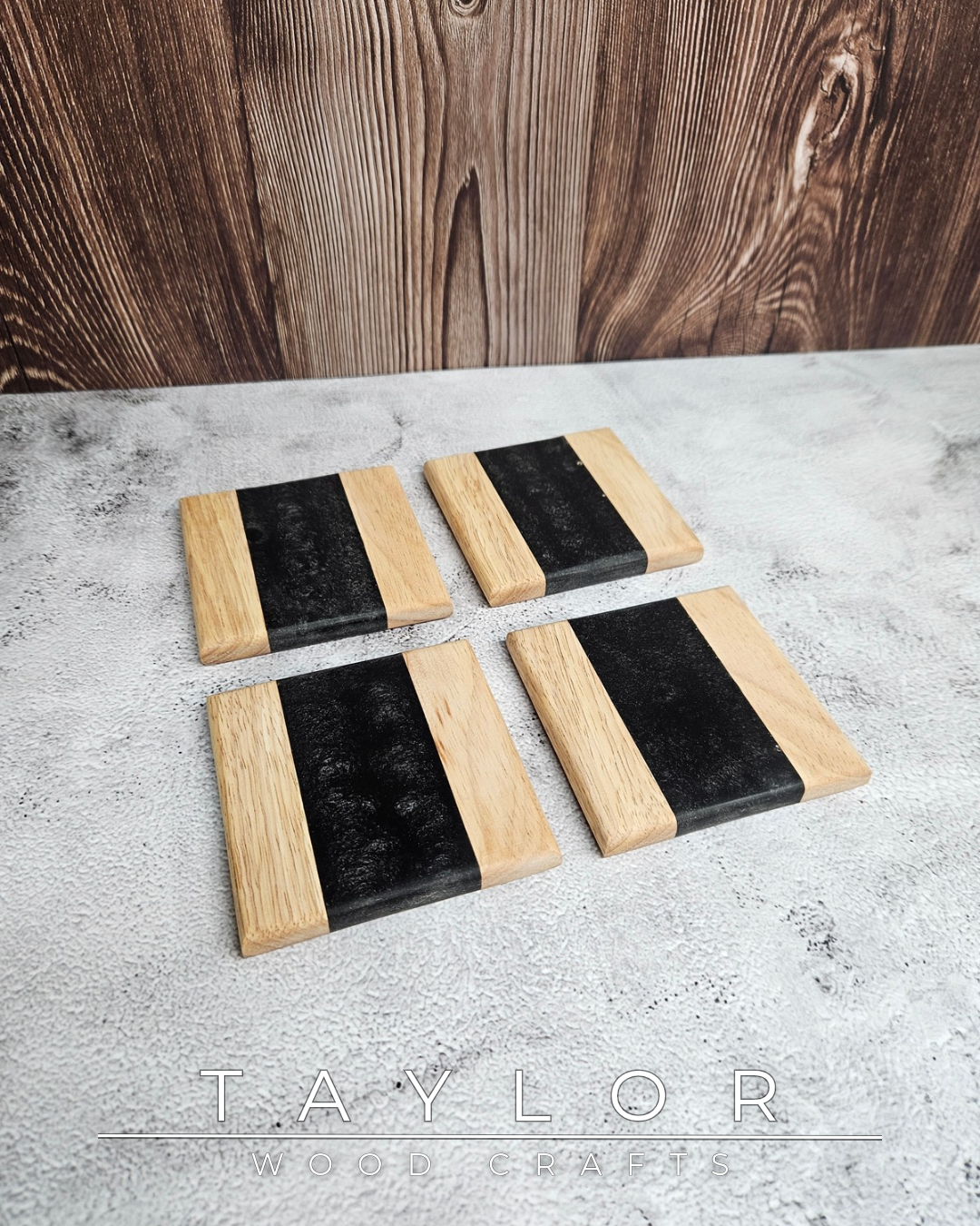 Set of four black and wood coasters on a gray surface with a wooden background.