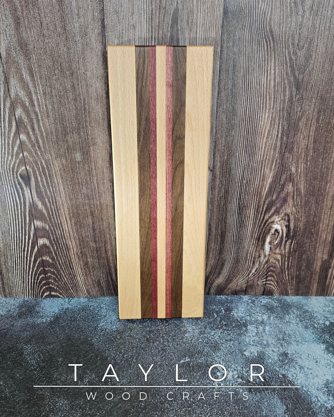 Wooden cutting board with multicolored stripes on a wooden surface, branded 'Taylor Wood Crafts'.