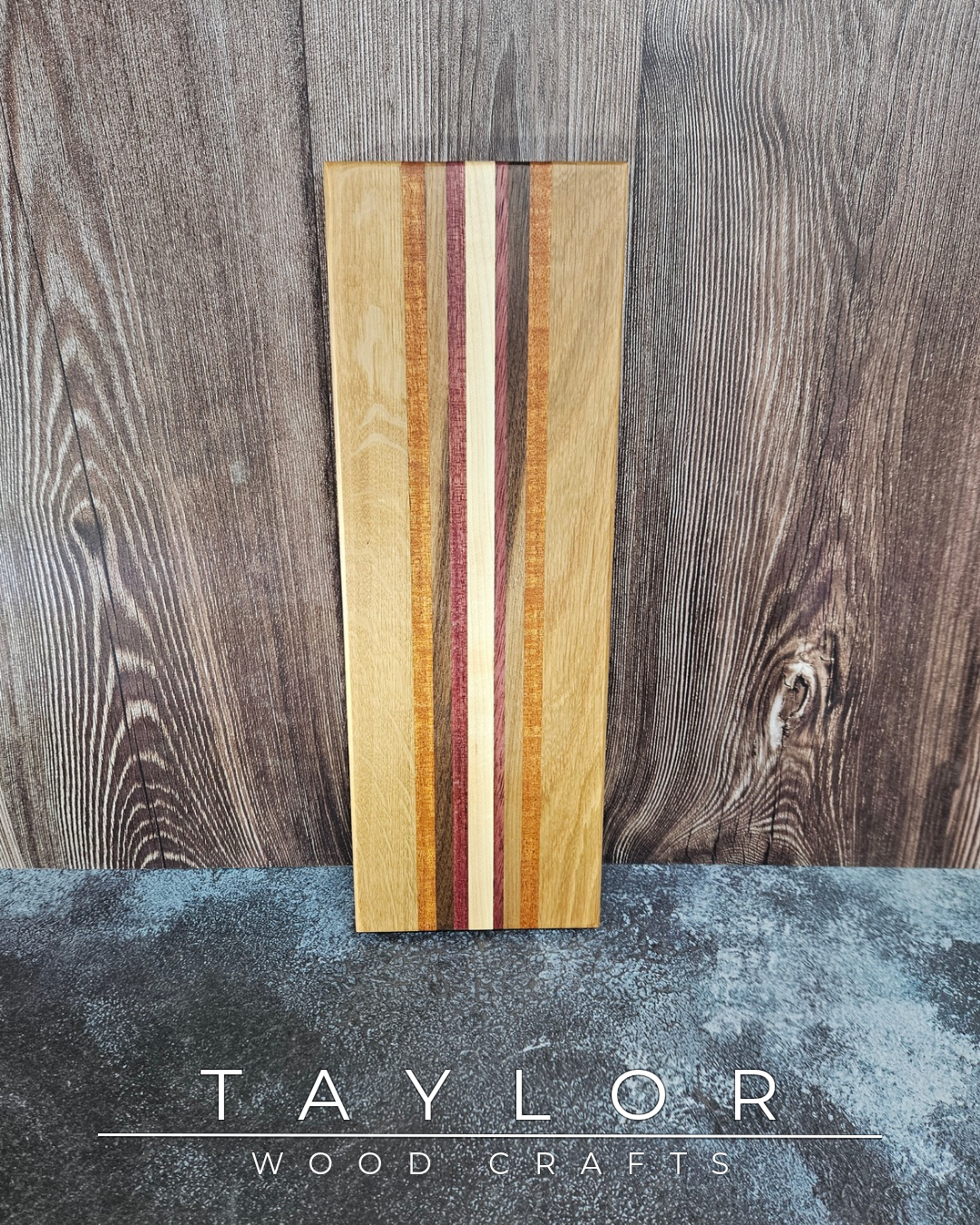 Wooden cutting board with multicolored stripes on a wooden surface, branded 'Taylor Wood Crafts'.