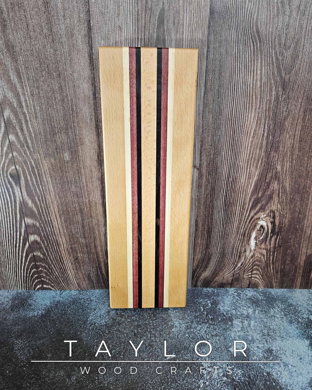 Wooden cutting board with striped design on a wooden surface, branded 'Taylor Wood Crafts'.