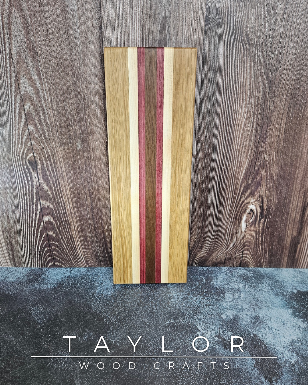 Wooden cutting board with multicolored stripes on a wooden background, featuring the brand 'Taylor Wood Crafts'.