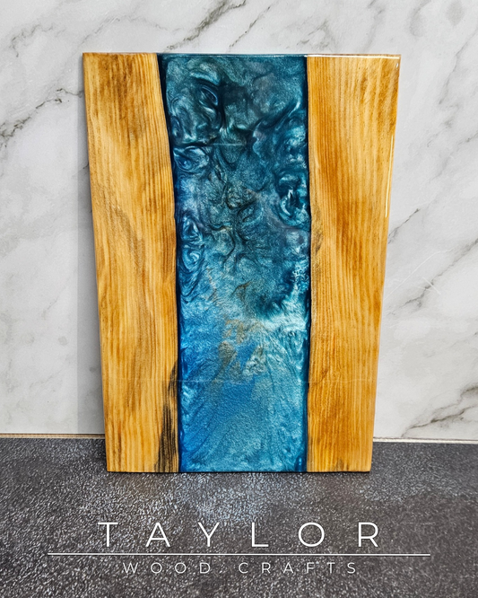 Wooden cutting board with blue resin inlay on a marble and stone surface, branded 'Taylor Wood Crafts'.